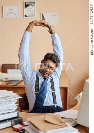 Businessman Stretching Arms at Office Desk Feeling Relaxed Businessman Stretching Arms at Office Desk Feeling Relaxed 117542427