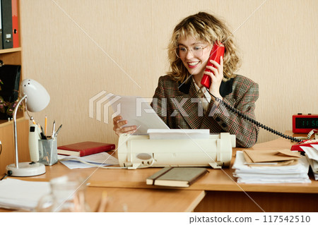 Smiling Businesswoman Speaking on Retro Red Rotary Phone 117542510