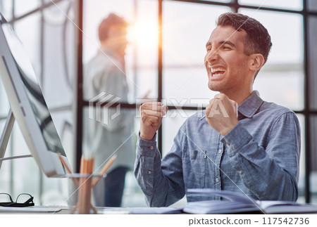 Happy businessman rejoicing success at workplace in office, looking at laptop screen with euphoric expression. Happy businessman rejoicing success at workplace in office, looking at laptop screen with euphoric expression. 117542736