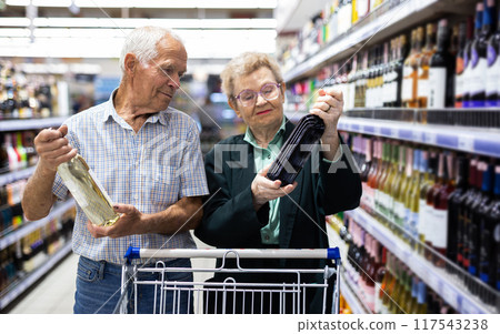 Mature couple chooses bottle of wine in alcohol section of supermarket 117543238