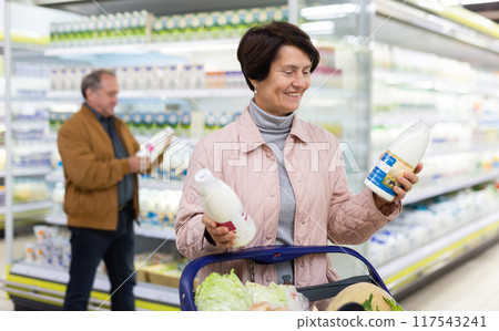 Mature couple choosing jug of milk in dairy department in grocery store 117543241