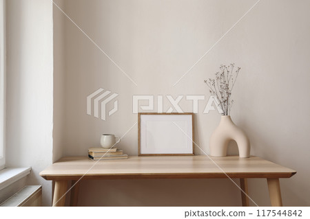 Horizontal empty wooden picture frame mockup. Boho shaped vase, dry flowers on table. Cup of coffee, old books. Working space, home office. Art, poster display. Modern interior. Beige wall background. Horizontal empty wooden picture frame mockup. Boho shaped vase, dry flowers on table. Cup of coffee, old books. Working space, home office. Art, poster display. Modern interior. Beige wall background. 117544842
