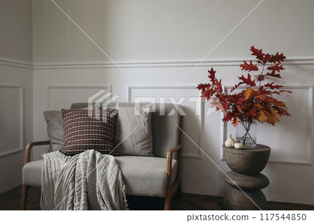 Red oak tree leaves, branches in vase on modern curved wooden side table. Linen midcentury sofa with throw blanket, checkered cushions. Little white pumpkins. Autumn interior, Thanksgiving, Halloween Red oak tree leaves, branches in vase on modern curved wooden side table. Linen midcentury sofa with throw blanket, checkered cushions. Little white pumpkins. Autumn interior, Thanksgiving, Halloween 117544850