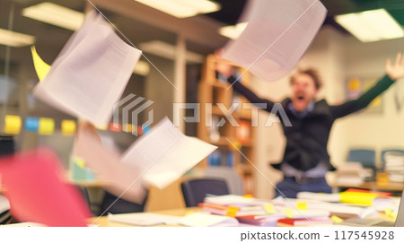 A businessman in a suit throws papers in the air in frustration, depicting a moment of stress in the office. Concept Intensity of workplace problems and emotional burnout associated with high pressure 117545928