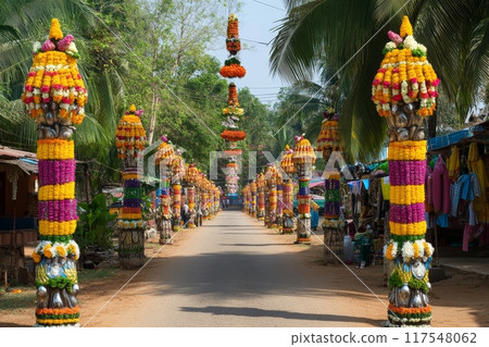 Vibrant floral decorations line a street during an Indian festival, with palm trees and shops in the background 117548062