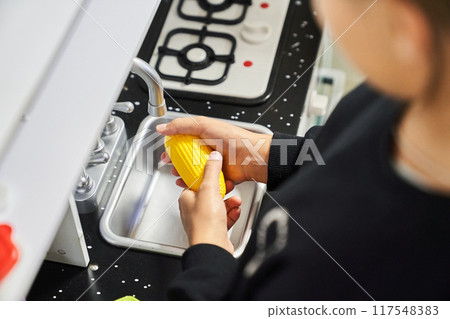 In the hands of a child lies a toy banana near the sink in the toy kitchen. With the ability to copy. The game of cooking. High quality photo In the hands of a child lies a toy banana near the sink in the toy kitchen. With the ability to copy. The game of cooking. High quality photo 117548383