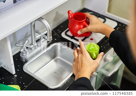 An unrecognizable girl is playing with plastic vegetables, with a toy kitchen in a nursery or kindergarten with space to copy. High quality photo 117548385