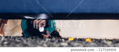 Girl with a flashlight looking under the bed. Girl with a flashlight looking under the bed. 117548404