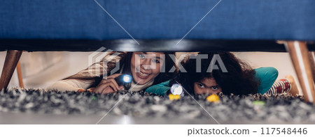 Woman and little girl with a flashlight looking under the bed. 117548446