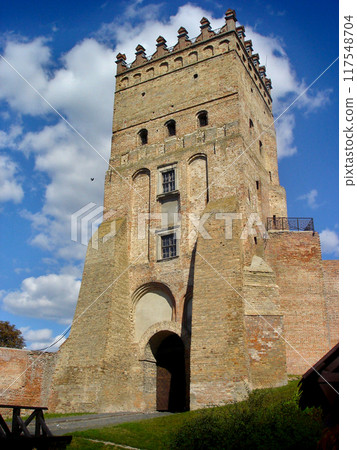 Entrance tower made of bricks of the medieval castle of Prince Lubart. Tower against a background of blue sky with white clouds Entrance tower made of bricks of the medieval castle of Prince Lubart. Tower against a background of blue sky with white clouds 117548704