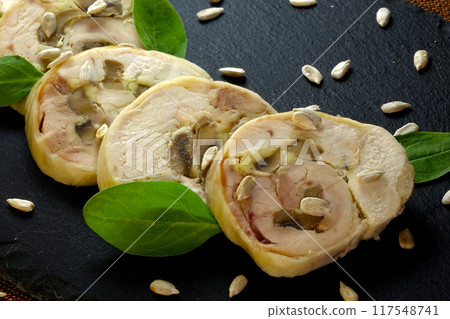 Meat Roll Slices Garnished With Spinach and Sunflower Seeds on a Black Ceramic Board 117548741