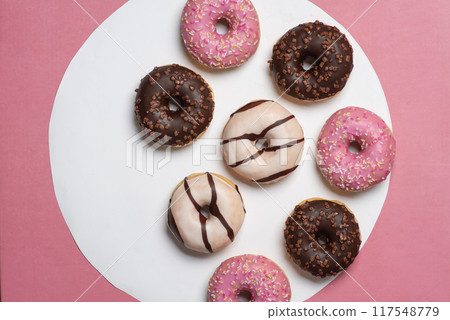 Colorful donuts with pink, chocolate, and white icing on white and pink background. 117548779