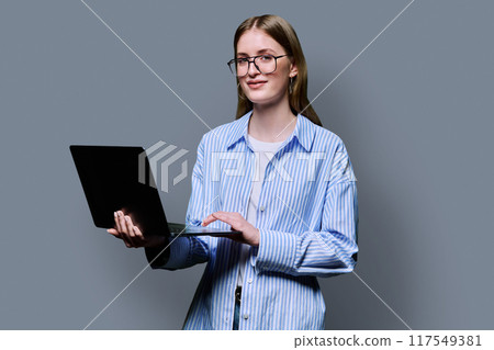Smiling teenage girl with laptop on grey studio background Smiling teenage girl with laptop on grey studio background 117549381