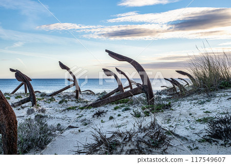 Rusty old anchors on the beach at the Anchor Cemetary graveyard at Praia do Barril beach in Tavira, Algarve, Portugal 117549607