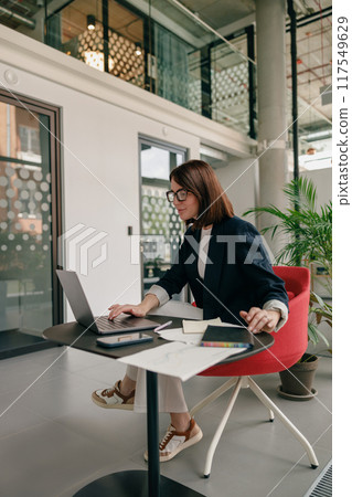 A businesswoman is focused on her work on a laptop in a modern office environment A businesswoman is focused on her work on a laptop in a modern office environment 117549629