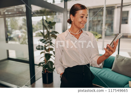 A professional woman is actively engaging with her smartphone while in a modern workspace setting 117549665