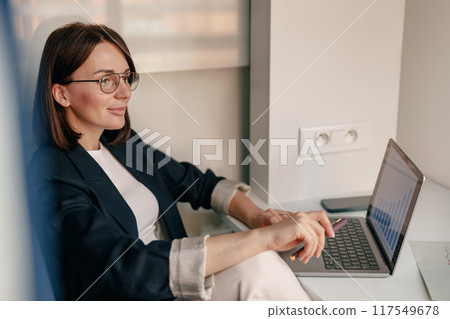 Confident businesswoman working on laptop in a modern office, showcasing dedication and efficiency 117549678