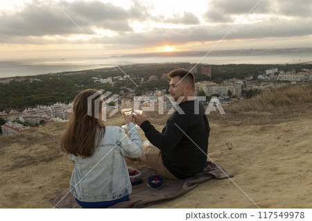 Loving couple having romantic picnic with wine at sunset overlooking city 117549978