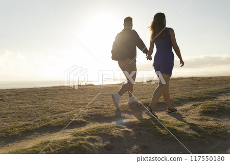 Loving couple walking on dirt path at sunset near ocean Loving couple walking on dirt path at sunset near ocean 117550180