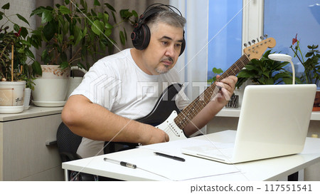 Man Wearing Headphones Learning to Play Guitar Online Man Wearing Headphones Learning to Play Guitar Online 117551541