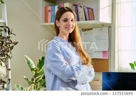 Portrait of smiling female teenager looking at camera with crossed arms in home Portrait of smiling female teenager looking at camera with crossed arms in home 117551693