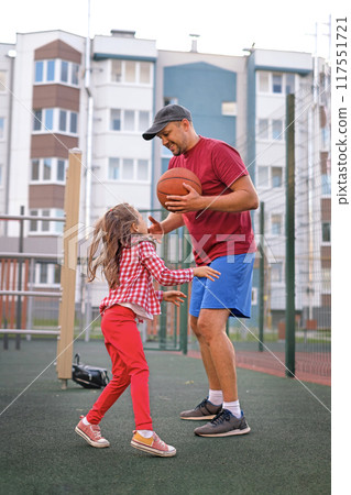 Dad teaches his little daughter to play basketball in the backyard. 117551721