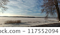 A snowy lake with trees in the foreground and blue sky behind 117552094