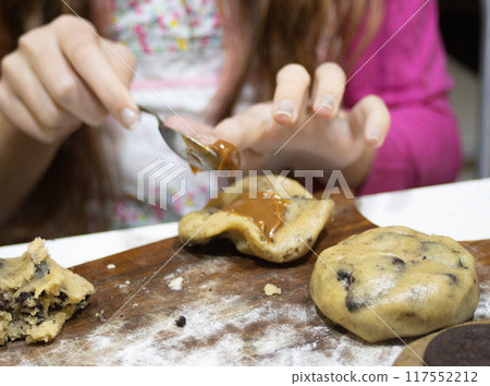 Closeup of girl's hands making filled cookies . Out of focus background.  117552212