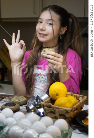 A girl baking cookies in her home kitchen and making a taste approval gesture. 117552213