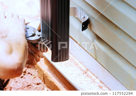 Worker cutting aluminum rain gutter with metal shears. Worker cutting aluminum rain gutter with metal shears. 117552294