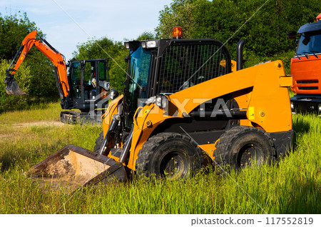 Two small excavators next to a truck. A new generation of special equipment at an open location on a sunny day Two small excavators next to a truck. A new generation of special equipment at an open location on a sunny day 117552819