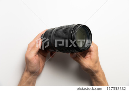 Horizontal shot of a camera lens on the hands of a man holding a zoom telephoto lens 117552882