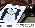 A clipboard holding a prenuptial agreement with a cut-out silhouette of a couple and wedding rings, next to a judge's gavel. 117553382