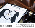 A clipboard holding a prenuptial agreement with a cut-out silhouette of a couple and wedding rings, next to a judge's gavel. 117553383