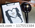 A clipboard holding a prenuptial agreement with a cut-out silhouette of a couple and wedding rings, next to a judge's gavel. 117553384