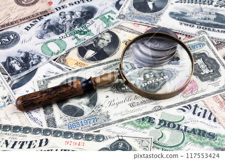 Old west US banknotes and silver certificates with silver dollar coins and magnifying glass 117553424