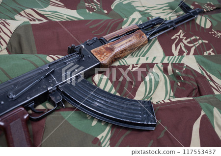 AK assault rifle on camo uniform background 117553437