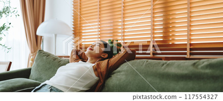 Relaxed young Asian woman enjoying rest on comfortable sofa 117554327