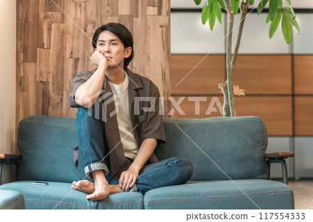 一個年輕的亞洲男子在客廳裡度過無聊的時光（無聊、沮喪、昏昏欲睡、遲鈍、疲倦、憤怒） 117554333