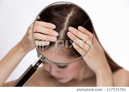 A woman's scalp is magnified with a magnifying glass. A woman's scalp is magnified with a magnifying glass. 117555781