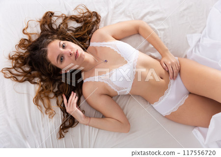 Cute girl in lingerie lounging on white sheets Cute girl in lingerie lounging on white sheets 117556720