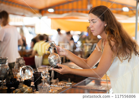 Girl in flea market store look at silver decanter, antique gifts 117556806