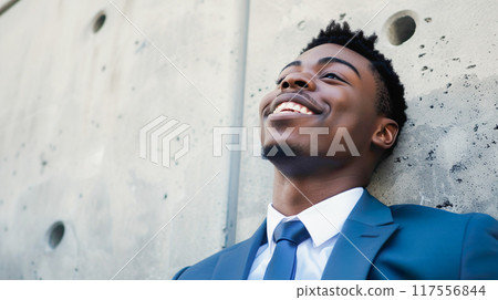 穿著西裝的黑人靠在混凝土牆上，微笑著抬頭 117556844