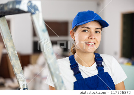 Smiling young female builder in blue uniform at construction site Smiling young female builder in blue uniform at construction site 117556873