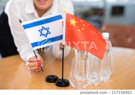 Unrecognizable girl sets midget flags of China and Israel before international negotiations 117556983