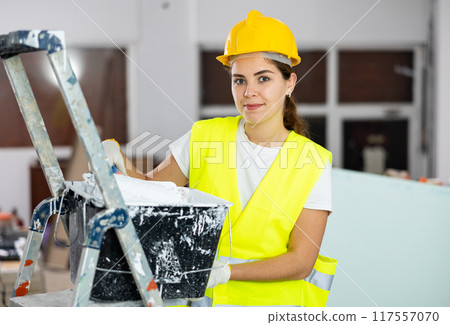 Portrait of woman painter in a protective helmet and vest with paint roller 117557070