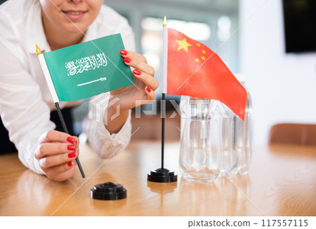 Unrecognizable girl sets midget flags of China and Saudi Arabia before international negotiations 117557115