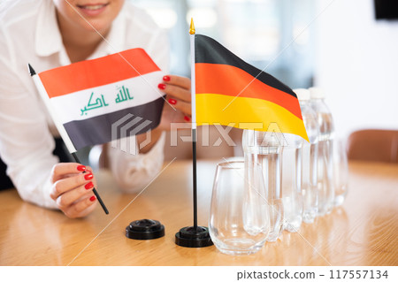 Little flag of Germany on table and flag of Iraq put next to it by young woman Little flag of Germany on table and flag of Iraq put next to it by young woman 117557134