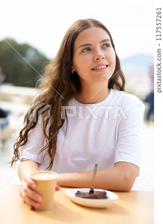 Portrait of a positive girl sitting at a table with a cup of delicious coffee 117557261