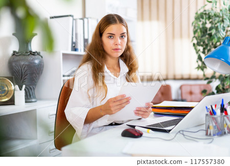 Focused young business woman working at office desk 117557380